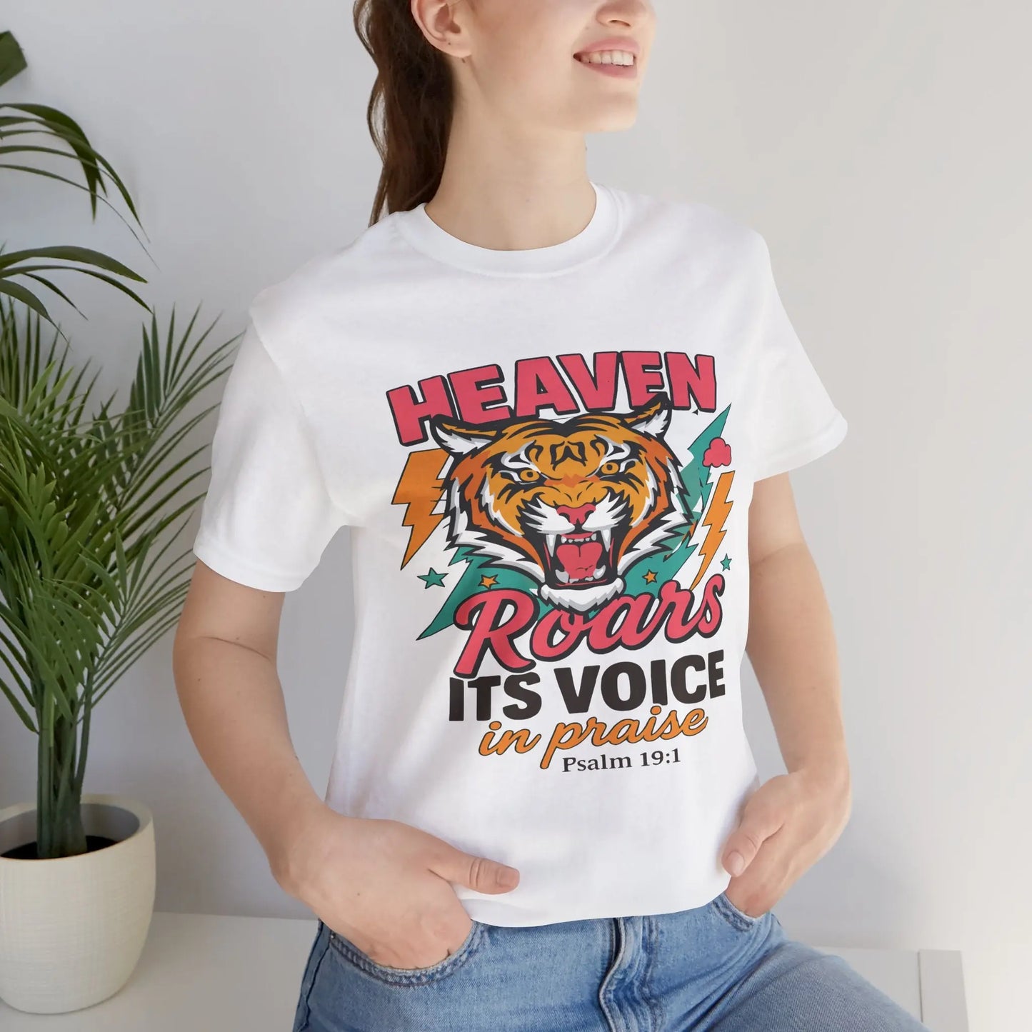Faith-inspired graphic t-shirt featuring a roaring tiger surrounded by lightning bolts, stars, and clouds, with bold typography reading “HEAVEN Roars ITS VOICE in praise – Psalm 19:1.” Vibrant colors and dynamic design celebrate divine power and praise.