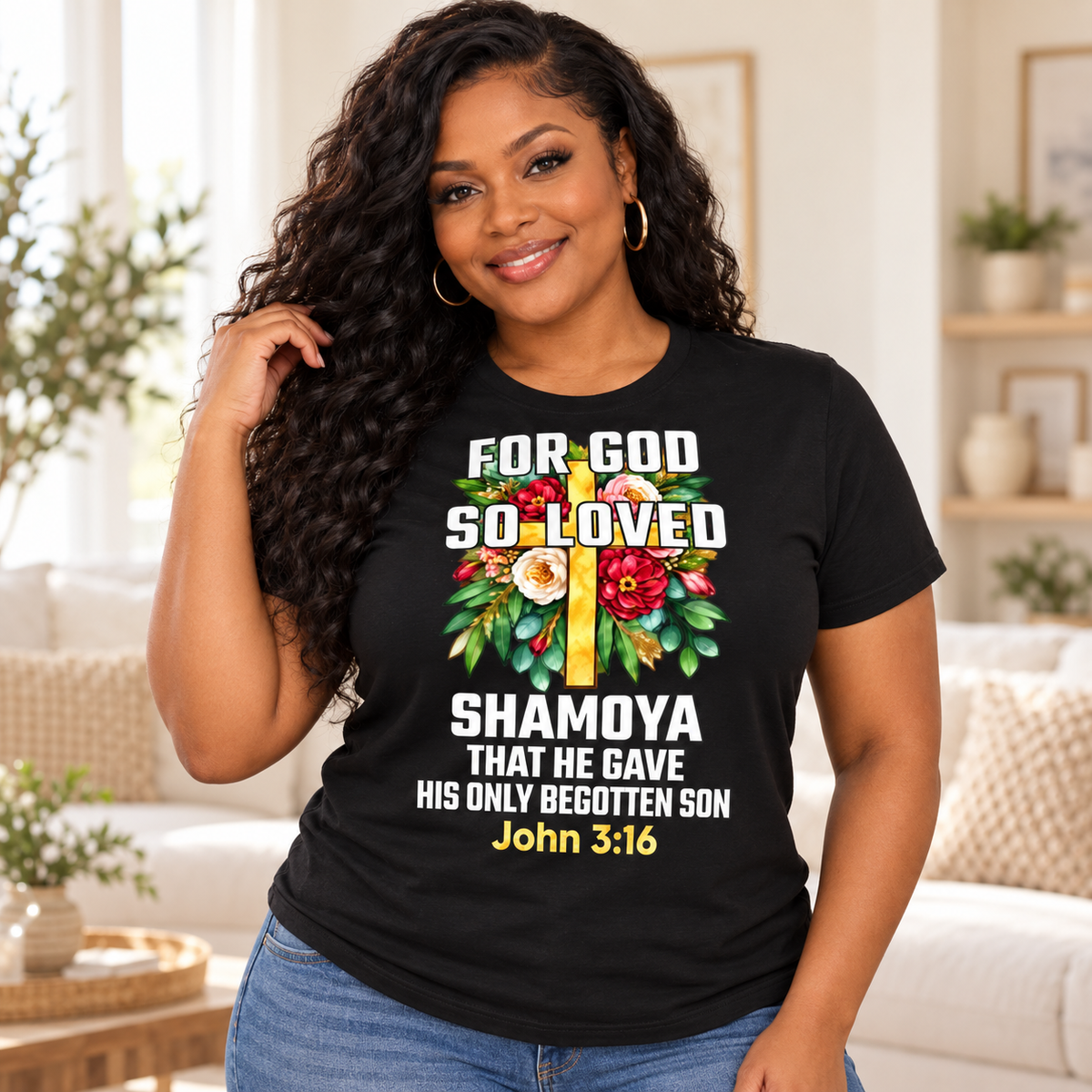 A woman wearing a black graphic t-shirt with a colorful floral cross design and the text 'FOR GOD SO LOVED SHAMoya THAT HE GAVE HIS ONLY BEGOTTEN SON John 3:16'.